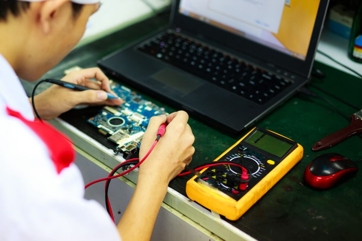 Pomiar multimetrem na płycie elektroniki obok laptopa diagnostycznego