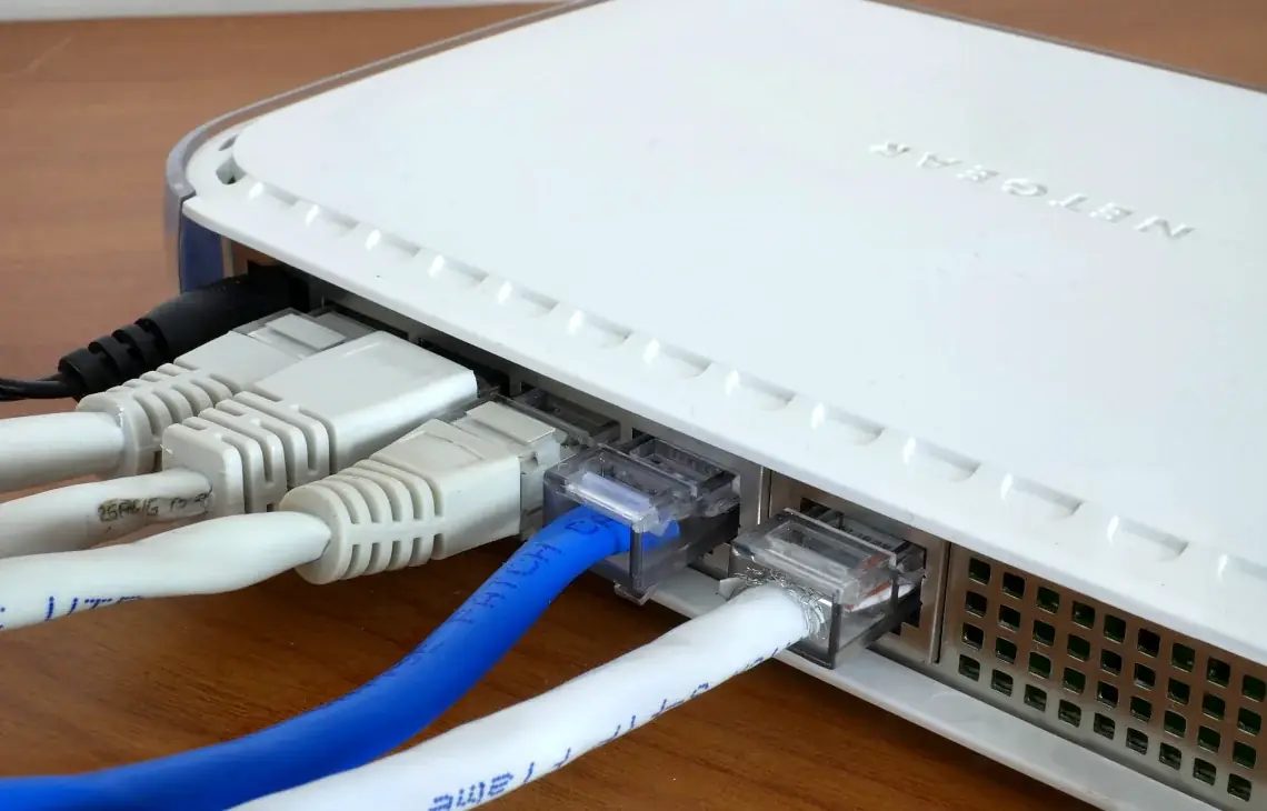 Router Netgear z podłączonymi kablami sieciowymi na drewnianym blacie