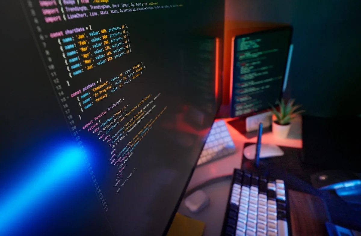 Kod programistyczny na ekranach komputera przy biurku ze stacją dokującą