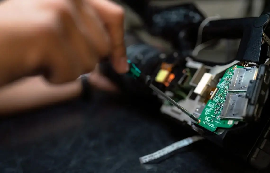 Dłoń naprawiająca płytę główną kamery/urządzenia elektronicznego z widocznym obwodem