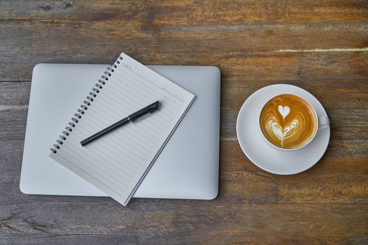 Zamknięty laptop, notes w linie i filiżanka kawy na drewnianym blacie