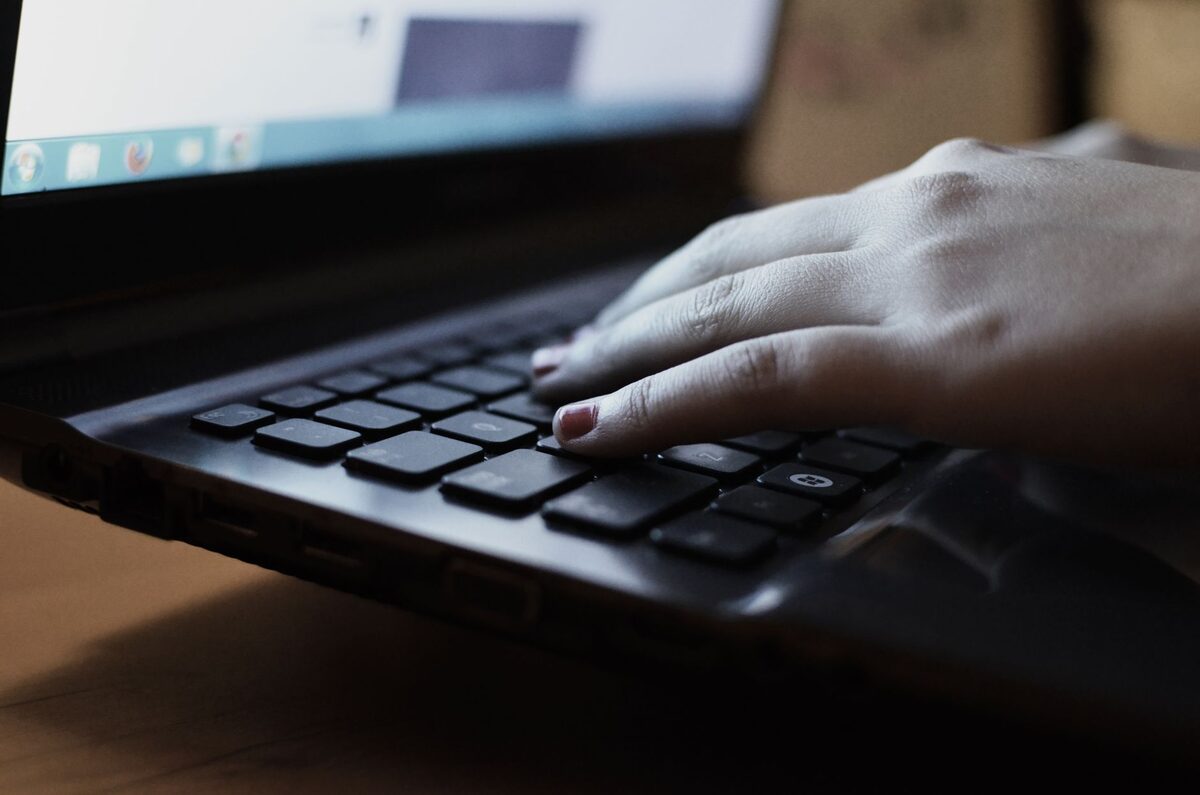 Dłoń pisząca na klawiaturze ciemnego laptopa