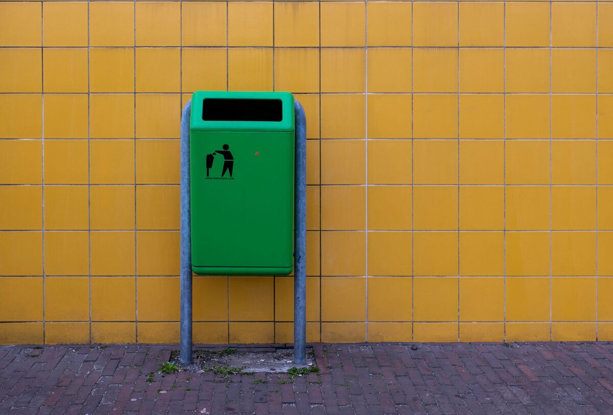 Zielony kosz na śmieci przy kaflowej ścianie