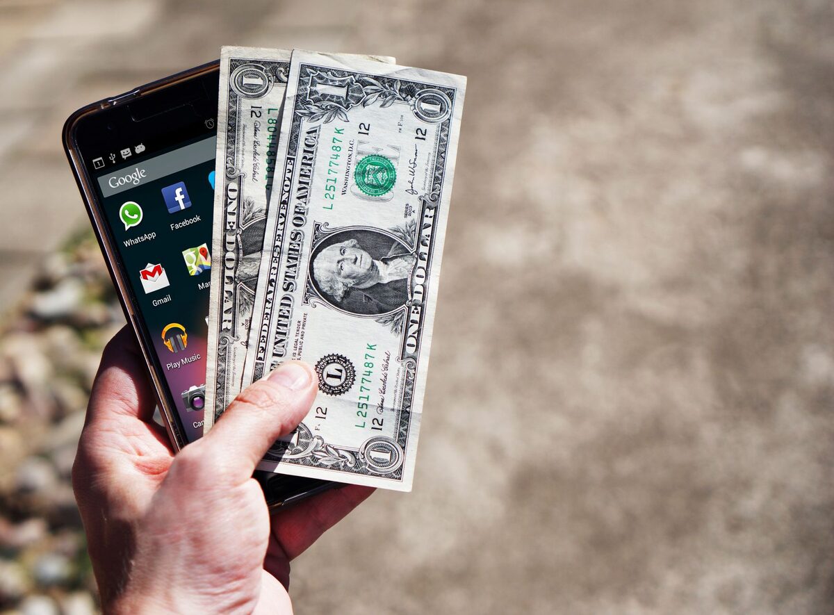Dłoń trzymająca telefon i banknot
